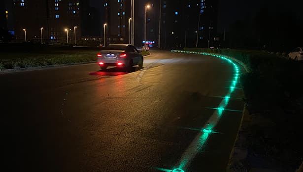 Green-lit solar road studs along curved road edge at night, guiding vehicle path